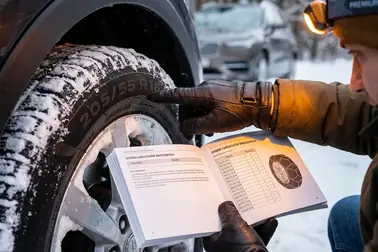 Kierowca porównujący zalecenia w instrukcji samochodu z oznaczeniem rozmiaru na boku opony