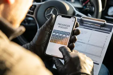 Kierowca sprawdzający prognozę pogody na telefonie podczas planowania wymiany opon