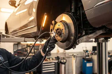 Mechanik diagnozujący zawieszenie i łożyska koła podczas przeglądu w profesjonalnym warsztacie samochodowym.