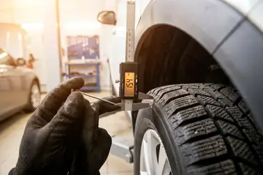 Mechanik mierzący miarką dostępny prześwit między oponą zimową a nadkolem auta.