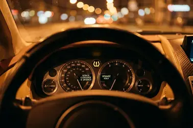 Świecąca na żółto kontrolka układu ostrzegania TPMS na desce rozdzielczej auta w nocy