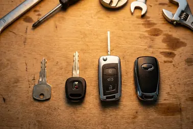 Klucz mechaniczny, klucz z transponderem, kluczyk składany i urządzenie systemu Keyless leżące na stole warsztatowym
