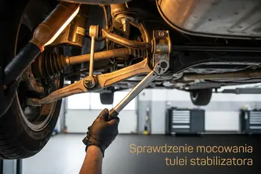 Mechanik kontrolujący drążek, tuleje i mocowania stabilizatora na podniesionym samochodzie