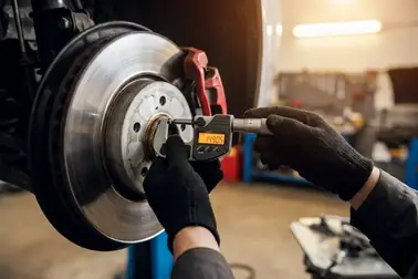 Mechanik warsztatu samochodowego mierzy grubość tarczy hamulcowej mikrometrem po naprawie usterki