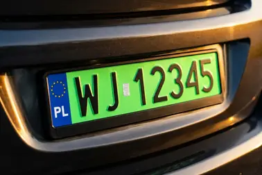 Polska tablica rejestracyjna z czarnymi znakami na zielonym tle na zderzaku auta