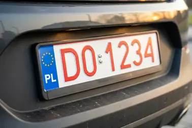 Polska tablica tymczasowa z czerwonym numerem na białym tle i niebieskim pasem PL