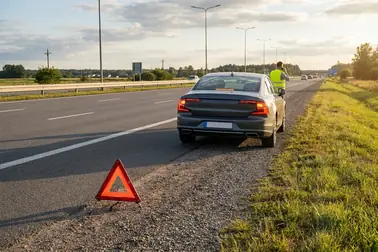 Samochód z włączonymi światłami awaryjnymi bezpiecznie zatrzymany na poboczu drogi.