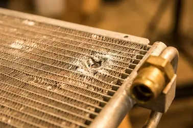 Skraplacz klimatyzacji z widocznym uszkodzeniem mechanicznym, korozją i podejrzanym połączeniem przewodu