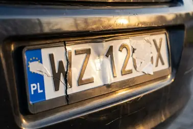 Wgnieciona tablica rejestracyjna z pęknięciem i ubytkiem powierzchni odblaskowej