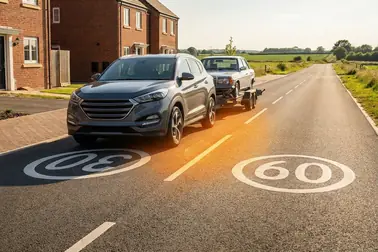 Samochód holujący drugie auto na drodze z zaznaczonymi limitami 30 km/h w obszarze zabudowanym i 60 km/h poza nim