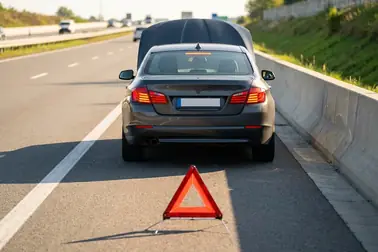 Samochód z włączonymi światłami awaryjnymi na poboczu autostrady i trójkąt ustawiony 100 metrów za nim