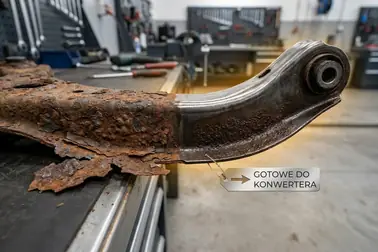 Stalowy element podwozia z powierzchniową korozją oraz fragmentem łuszczącej się rdzy wymagającej usunięcia